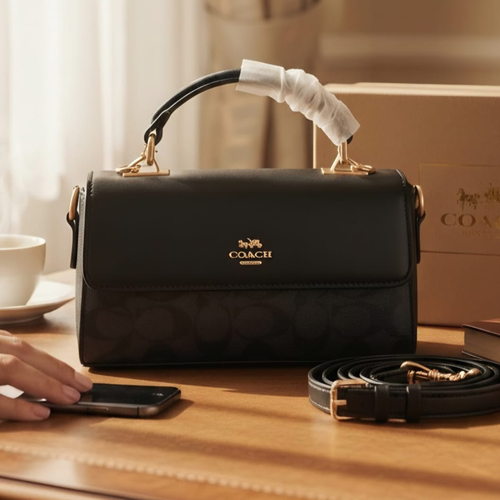 Coach Eliza foldover top handle bag black on wooden table with Coach box and coffee