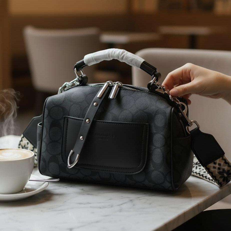 Coach Gotham duffle bag charcoal signature canvas on marble cafe table with woven geometric crossbody strap and coffee
