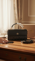 Coach Marlie top handle bag in black leather on wooden dresser with Coach box